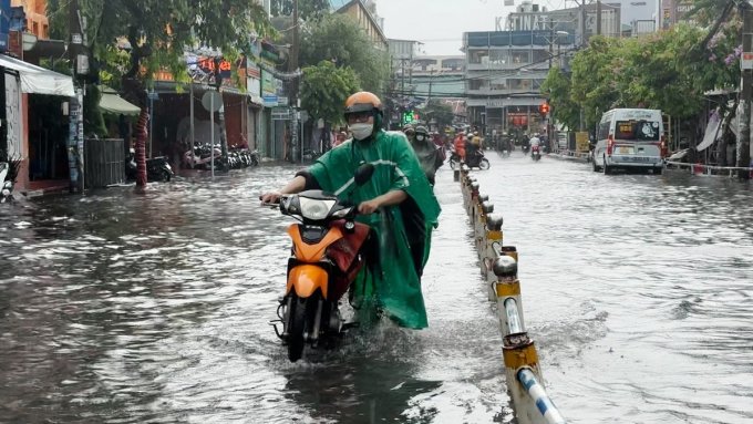 Người dân bì bõm dắt xe chết máy qua nước ngập nửa bánh xe sau cơn mưa lớn ở TP HCM. Ảnh:Đình Văn